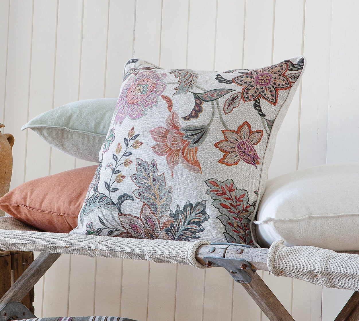 Decorative cushions on a bench with rustic vases against a white paneled wall