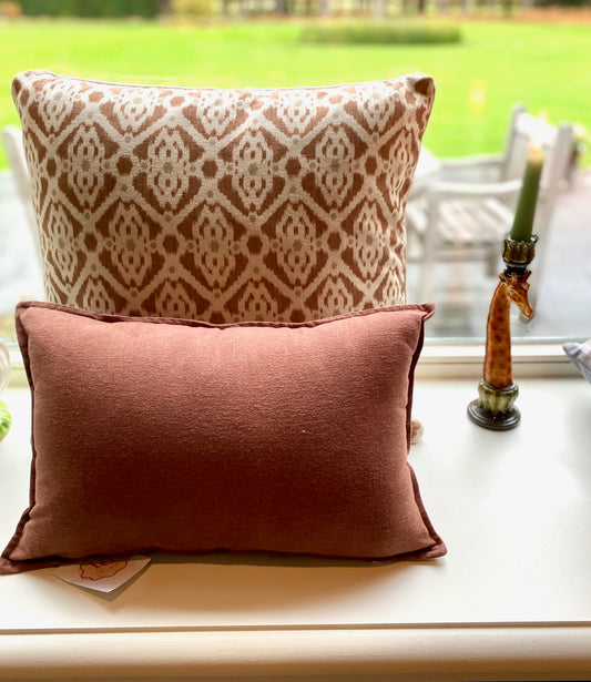Two patterned pillows on a windowsill with a garden view outside.