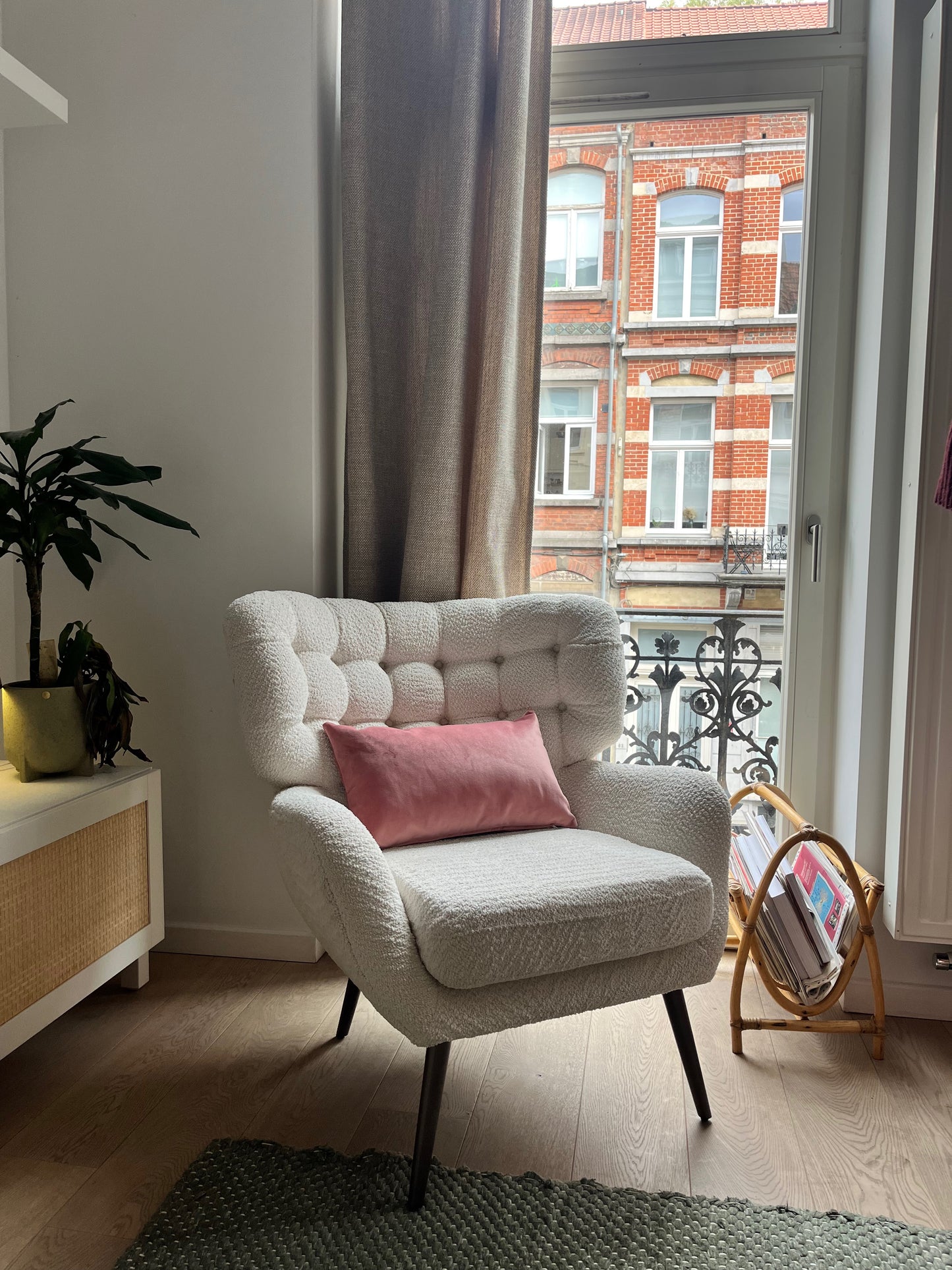 Gray armchair with a pink pillow in a room with a window and plant.