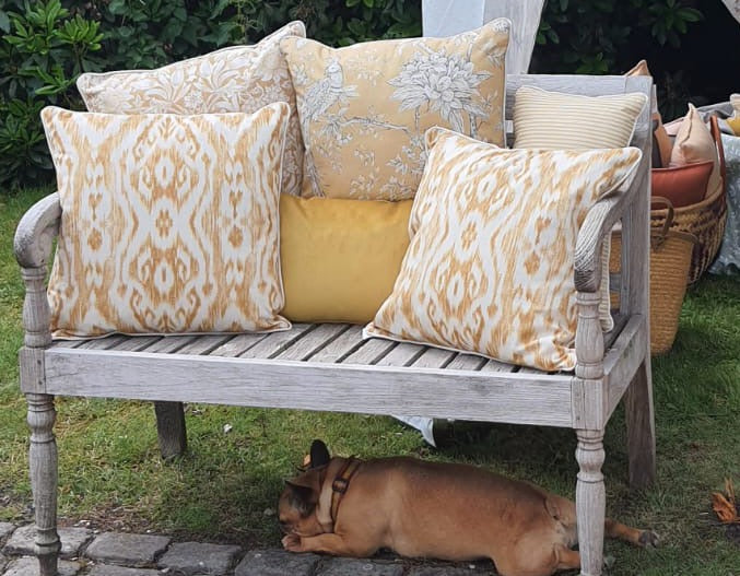 Decorative yellow linen pillows on a wooden bench with a dog lying on the ground.