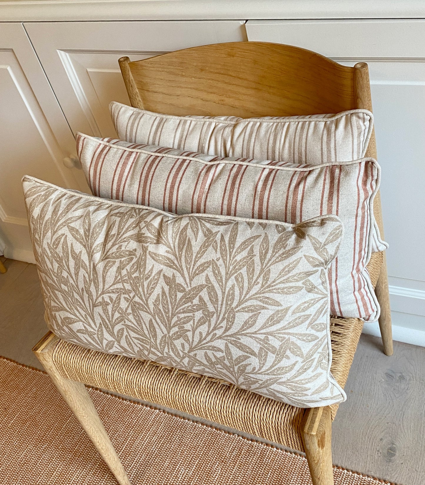 Three decorative pillows on a wooden chair with a neutral background