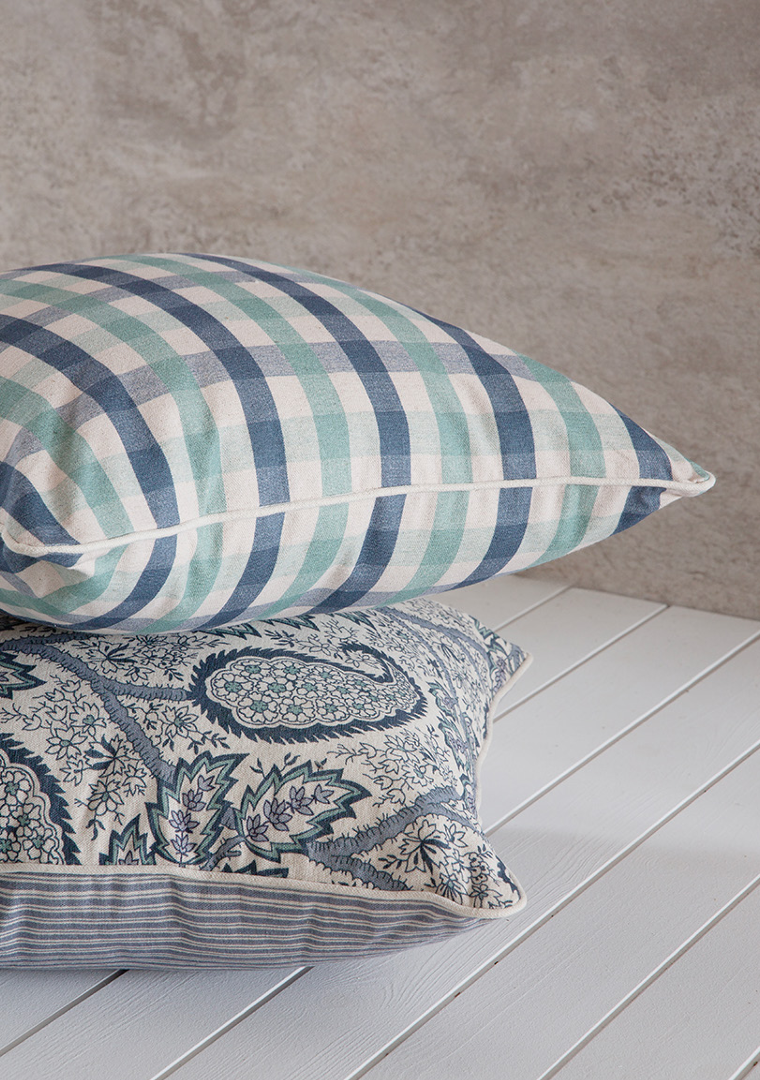 Two decorative pillows on a wooden surface with a neutral background. chekered blue and green pattern 50x50cm paisley pattern with piping in linen