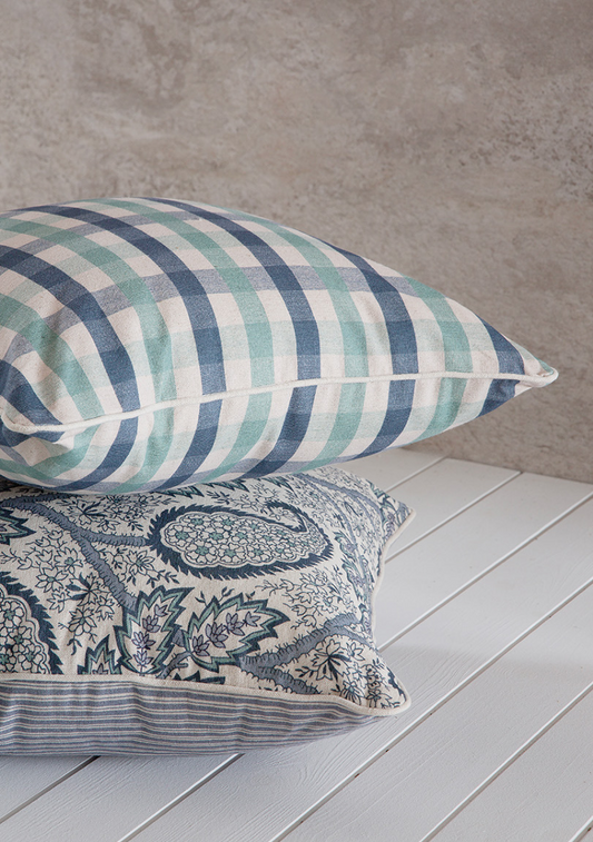 Two decorative pillows on a wooden surface with a neutral background. chekered blue and green pattern 50x50cm paisley pattern with piping in linen