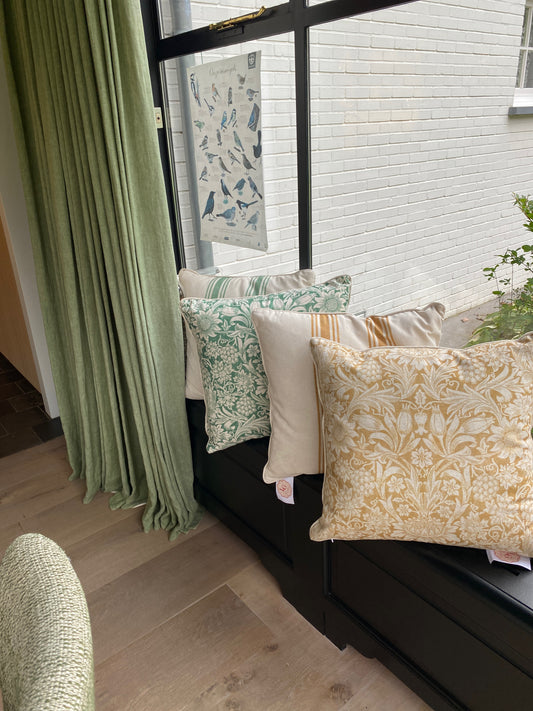 Decorative pillows on a bench by a window with green curtains