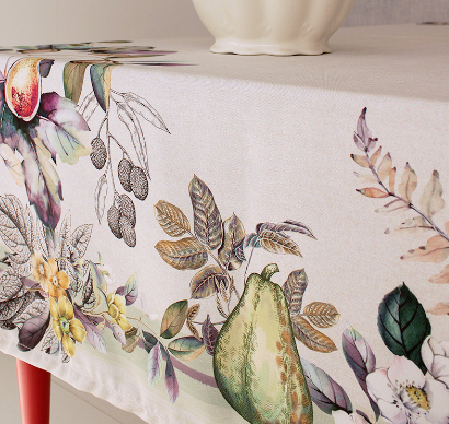 A tablecloth with a floral design, predominantly white with green and pink accents, displayed on a table along with a white vase with a floral design.