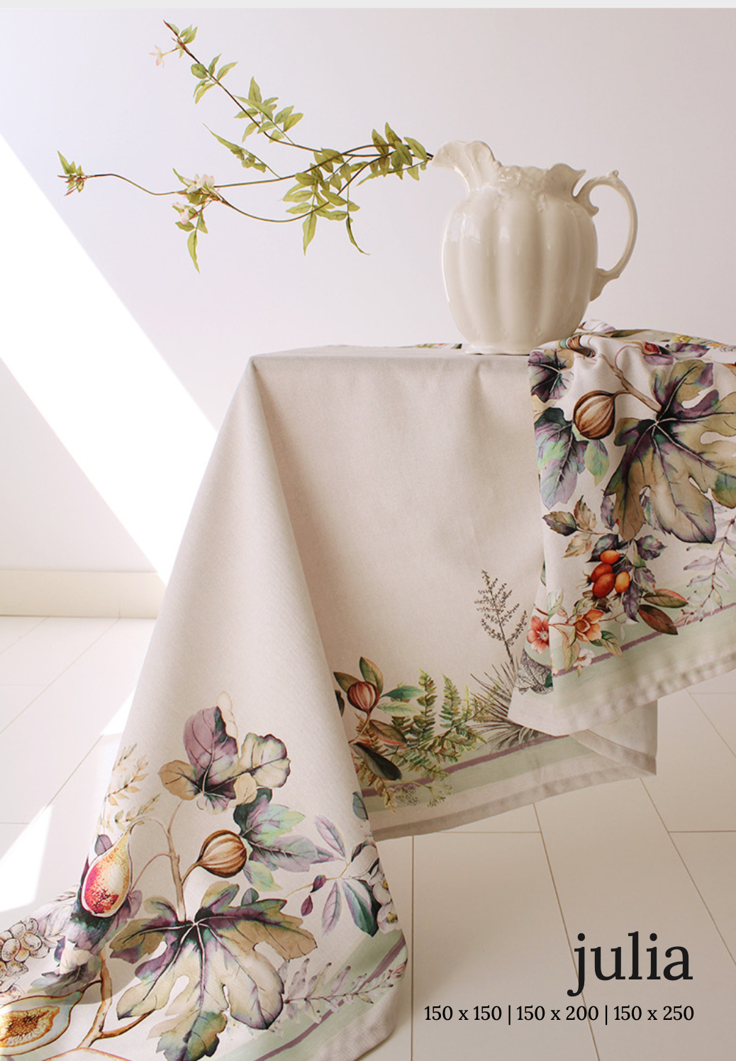 A tablecloth with a floral design, predominantly white with green and pink accents, displayed on a table along with a white vase with a floral design. New Classic