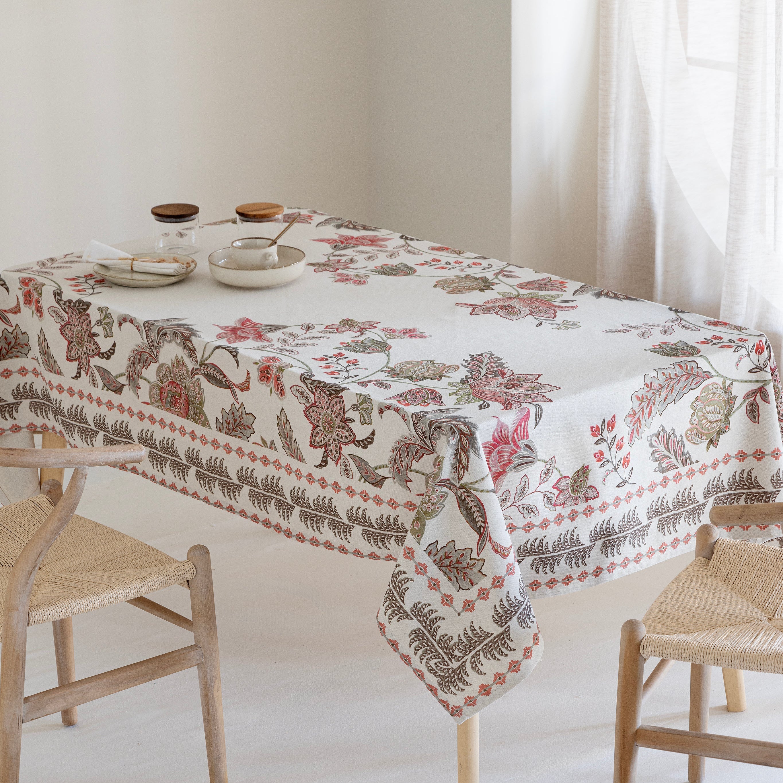Tablecloth with floral and leaf pattern on a table with chairs in a bright room.