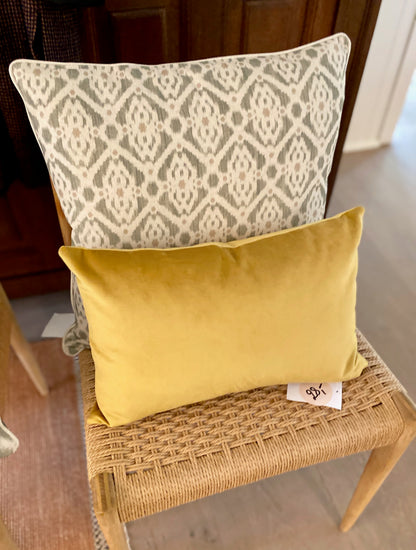 Two pillows, one patterned and one yellow, on a wicker chair.