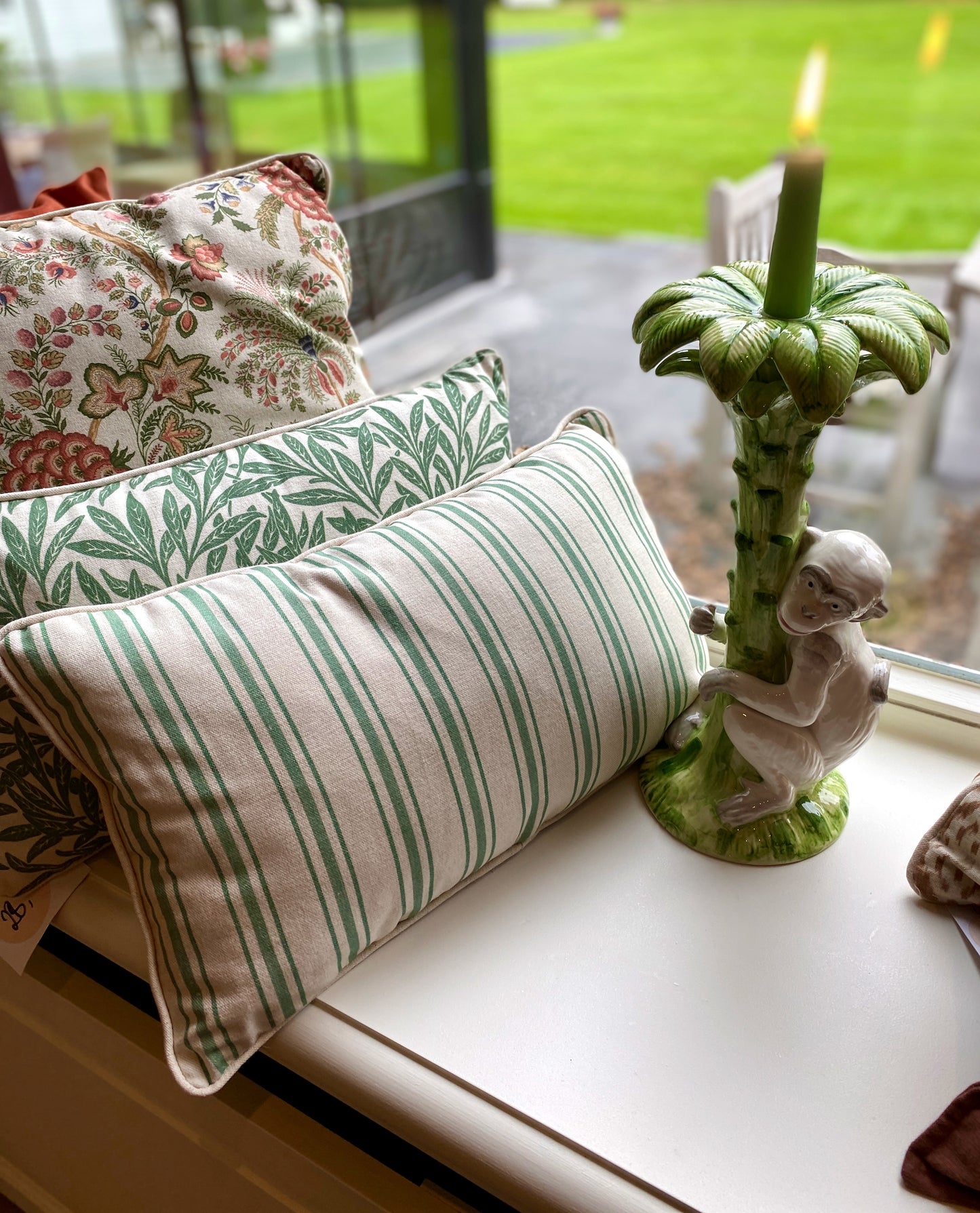 Decorative pillows with green and beige stripes on a windowsill with a candle holder.