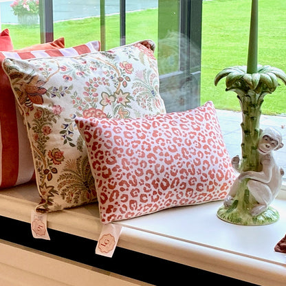 Decorative pillows with floral and leopard print on a windowsill with a view of greenery outside.