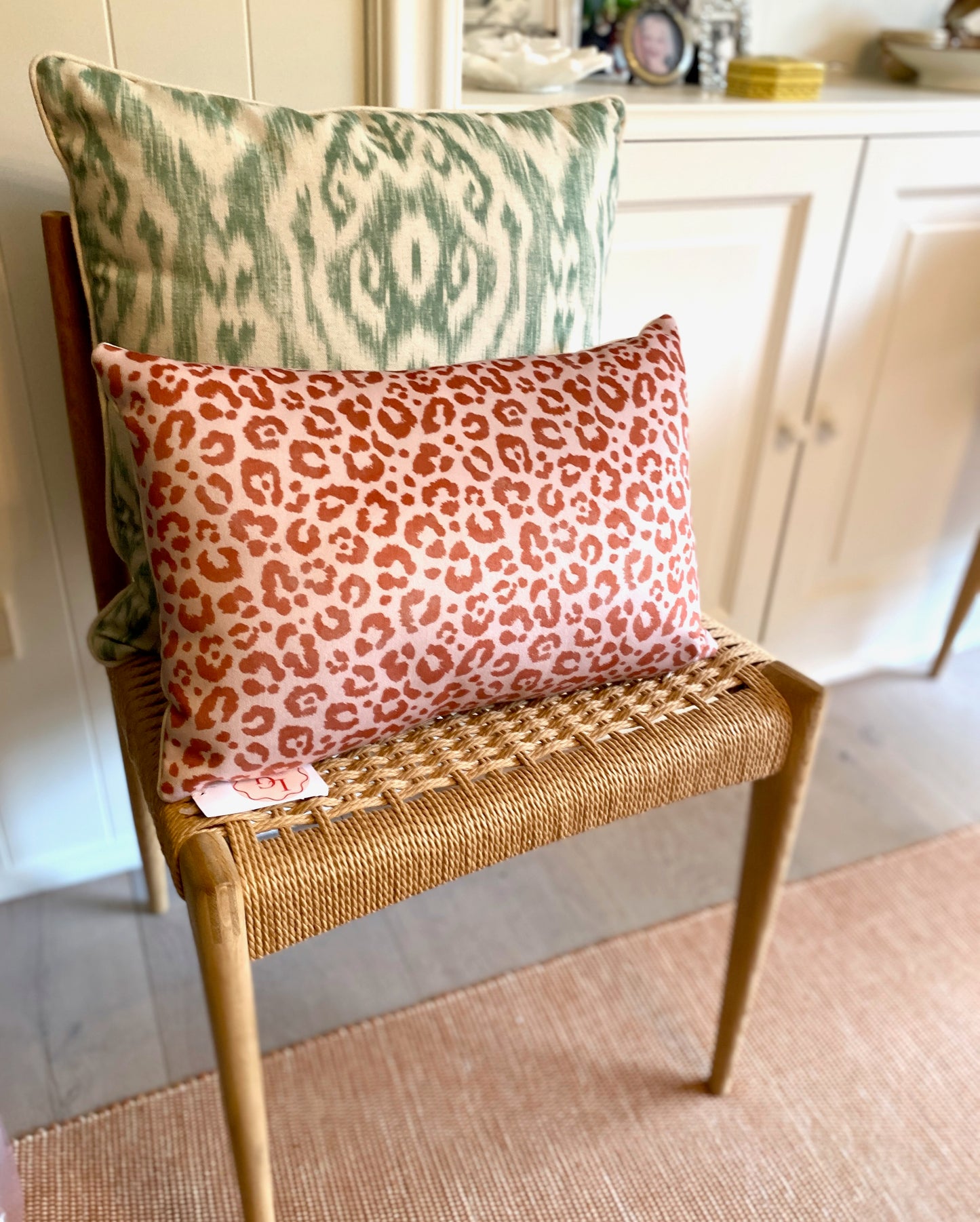 Two patterned pillows on a wicker chair in a home setting.