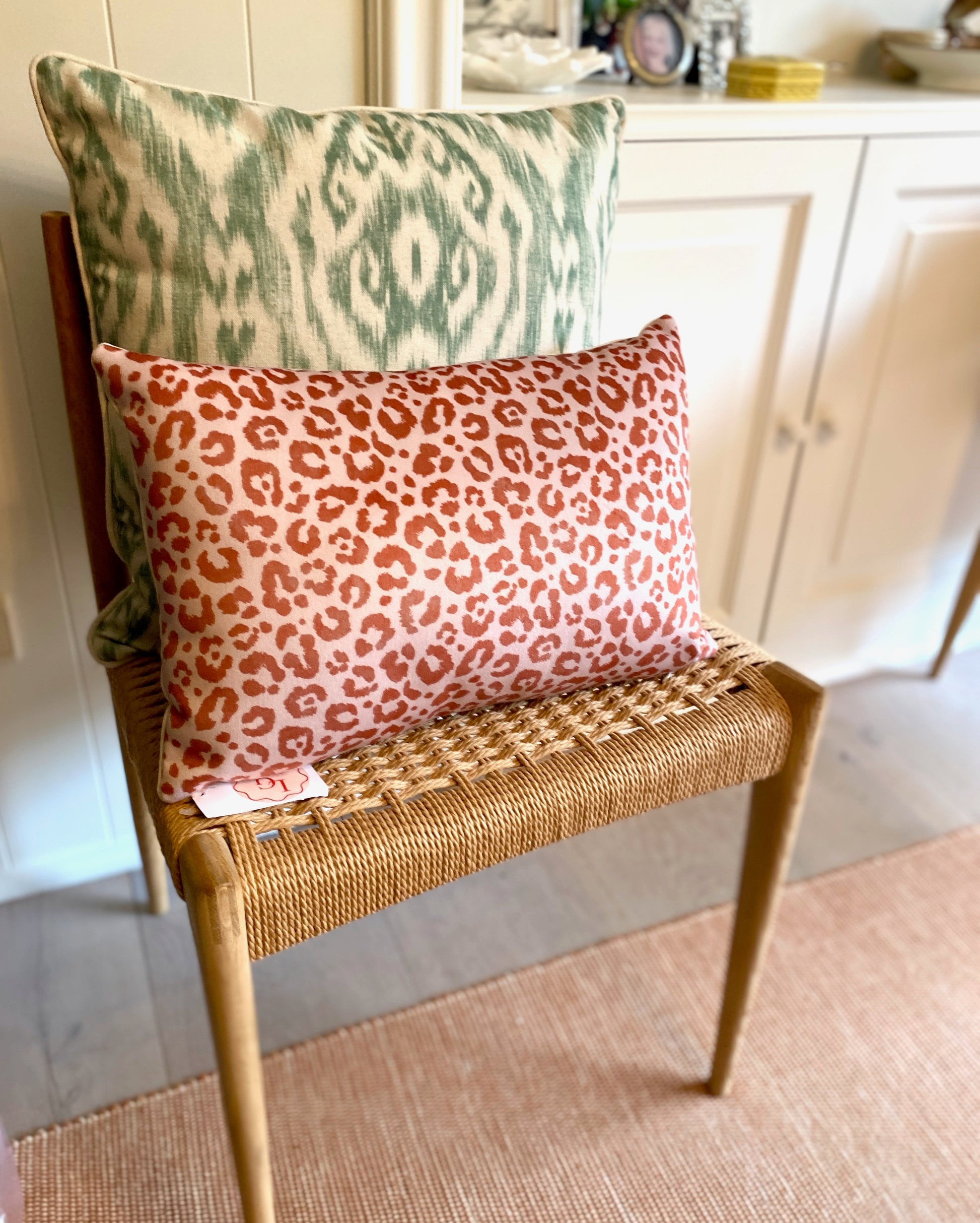 Two patterned pillows on a wicker chair in a home setting.