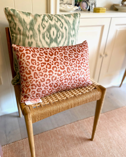 Two patterned pillows on a wicker chair in a home setting.