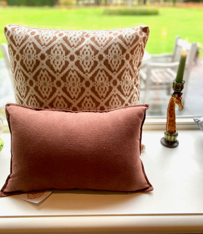Two patterned pillows on a windowsill with a garden view outside.