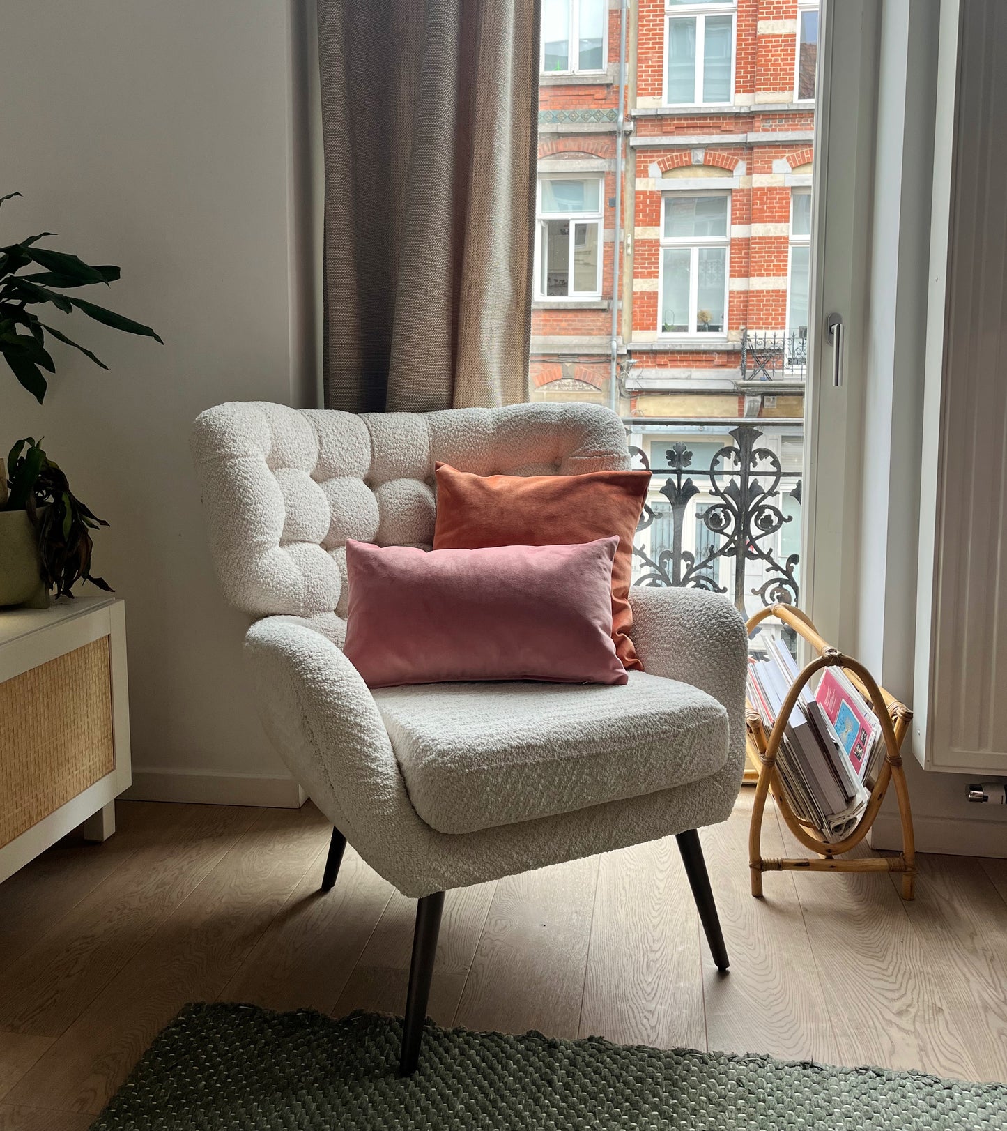 White armchair with pink cushions in a room with a window and plant