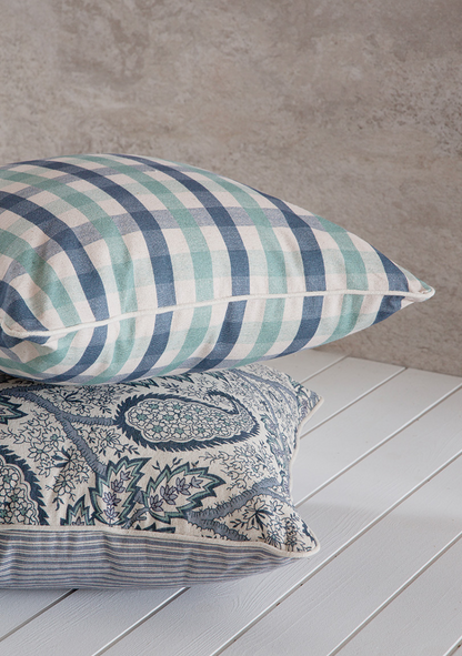 Two decorative pillows on a wooden surface with a neutral background. chekered blue and green pattern 50x50cm paisley pattern with piping in linen