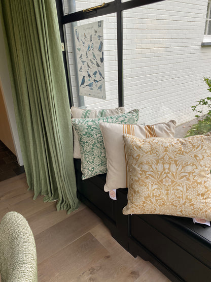 Decorative pillows on a bench by a window with green curtains