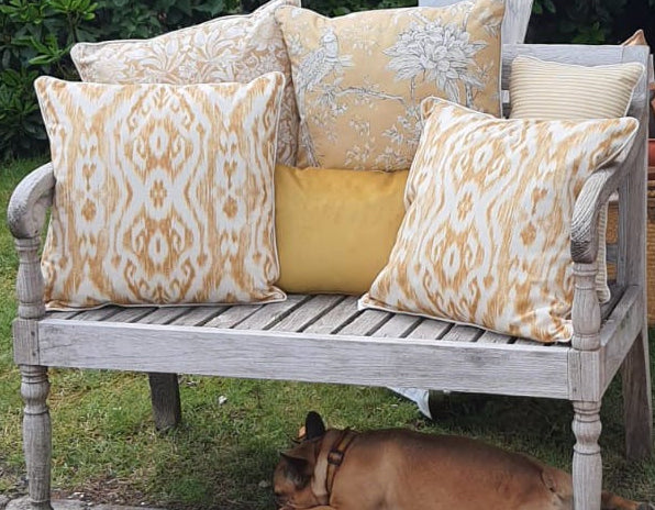 Decorative yellow pillows on a wooden bench with a dog lying on the grass.