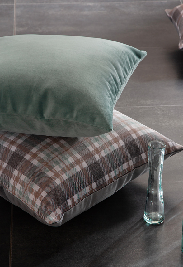 Two pillows, one green and one plaid, on a dark surface with a glass vase.