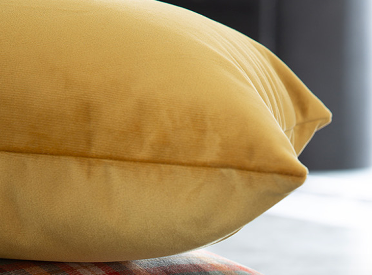 Close-up of a mustard yellow velvet pillow 45x45 cm on a blurred background